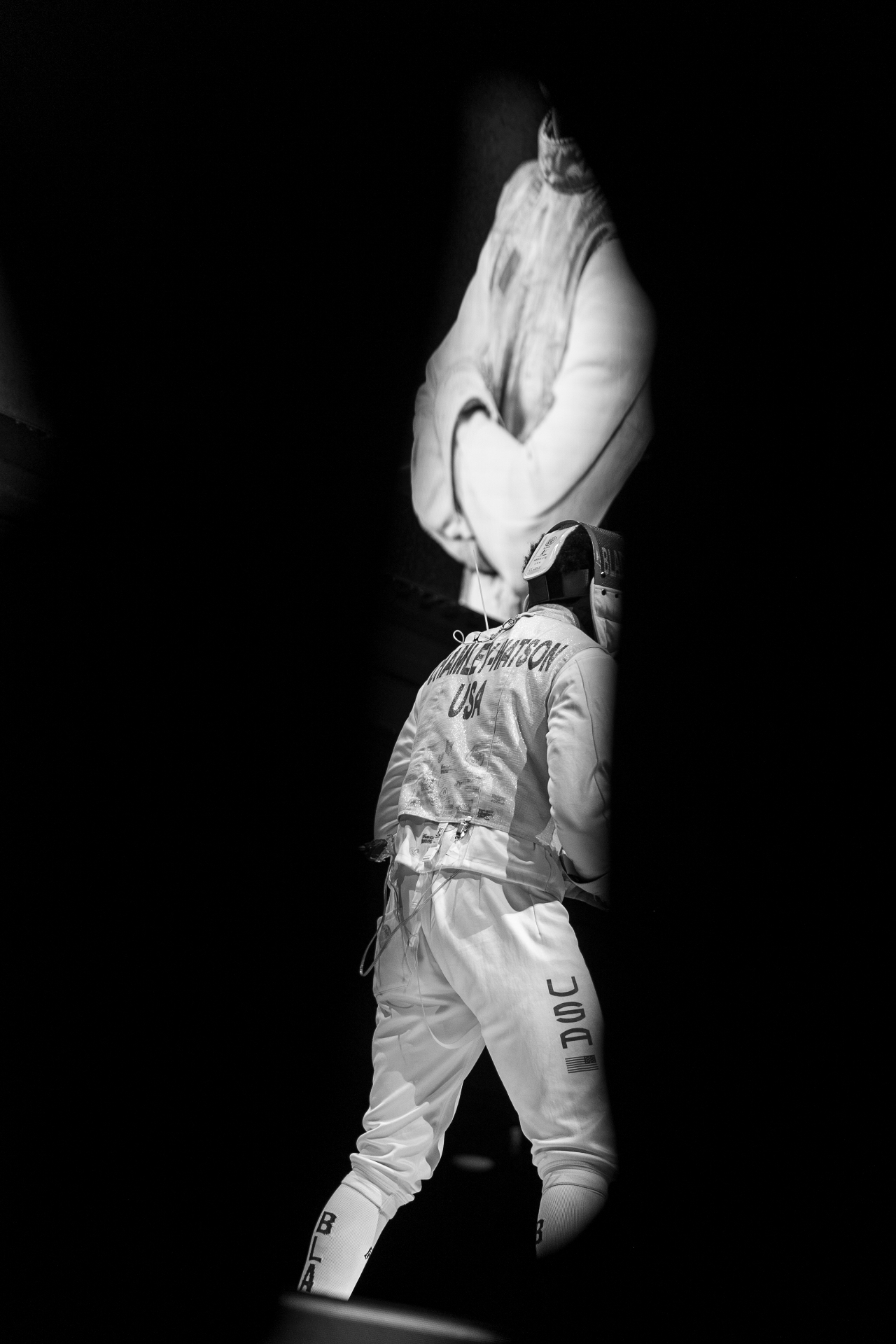 A Blade Collective fencer in a spotlit silhouette, walking into the arena.